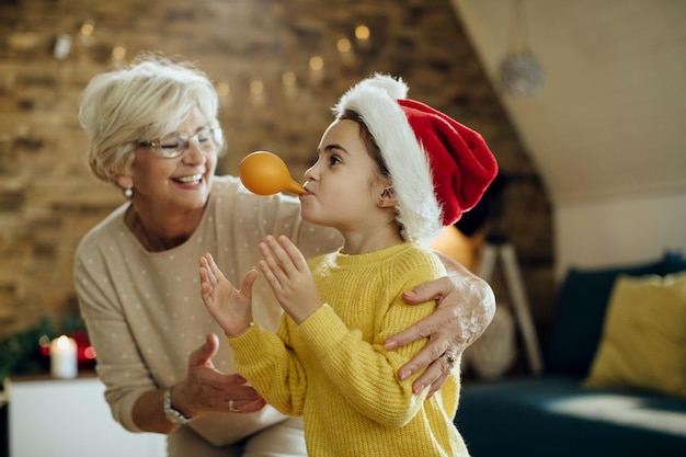 Bambina giocosa e sua nonna che soffiano palloncini e si divertono il giorno di Natale