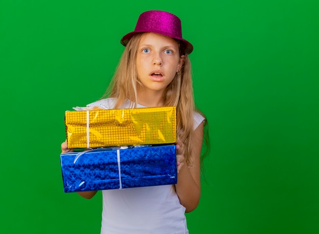 Bambina graziosa in cappello di festa che tiene i contenitori di regalo