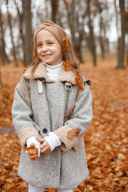 Bambina in abiti di moda in piedi nella foresta di autunno Ragazza in posa per una foto Ragazza che indossa un cappotto grigio e una fascia