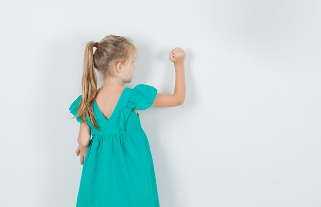 Bambina in abito verde guardando la parete, vista posteriore.
