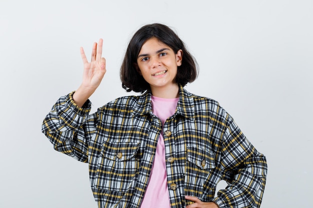 Bambina in camicia, giacca che mostra gesto ok e sembra felice, vista frontale.