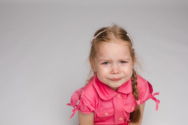 Bambina in camicia rosa che guarda da parte e piange su sfondo isolato Bambino triste spaventato che urla in studio Bambino infelice che piange Concetto di violenza offesa e infanzia