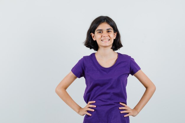 Bambina in maglietta che tiene le mani sulla vita e che sembra felice,