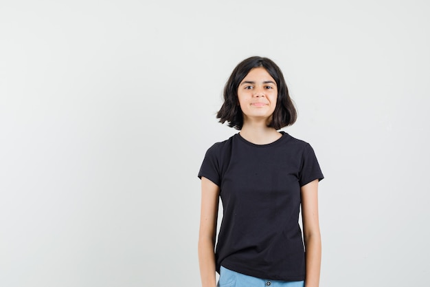 Bambina in maglietta nera, pantaloncini guardando davanti mentre sorride, vista frontale.
