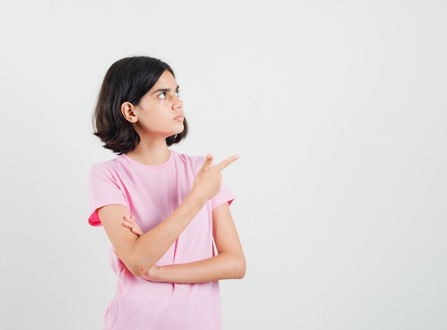 Bambina in maglietta rosa che punta all'angolo in alto a destra e che sembra concentrata, vista frontale.