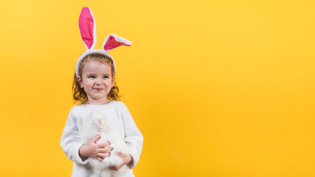Bambina in orecchie da coniglio in piedi con coniglio