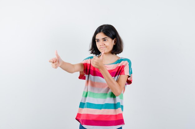 Bambina in t-shirt che mostra il doppio pollice in alto e sembra pensierosa, vista frontale.