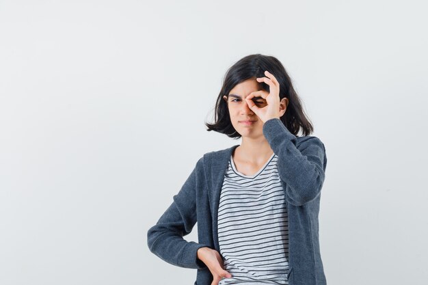 Bambina in t-shirt, giacca che mostra il segno giusto sull'occhio e che sembra sicura
