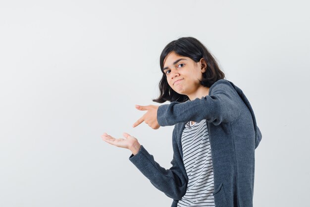 Bambina in t-shirt, giacca che punta al palmo vuoto e sembra sicura