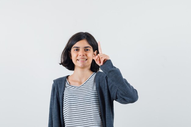 Bambina in t-shirt, giacca rivolta verso l'alto e che sembra allegra