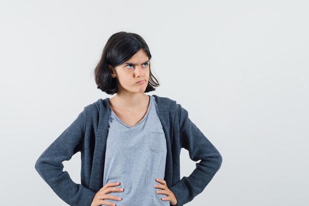 Bambina in t-shirt, giacca tenendo le mani sulla vita e guardando pensieroso