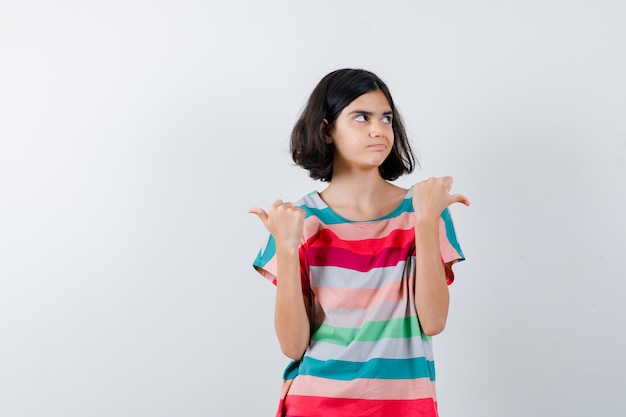 Bambina in t-shirt, jeans che punta a sinistra ea destra e sembra dispiaciuta, vista frontale.