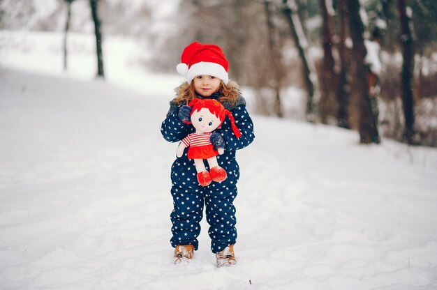 Bambina in un cappello blu che gioca in una foresta di inverno