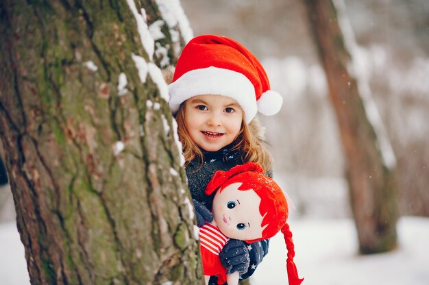 Bambina in un cappello blu che gioca in una foresta di inverno