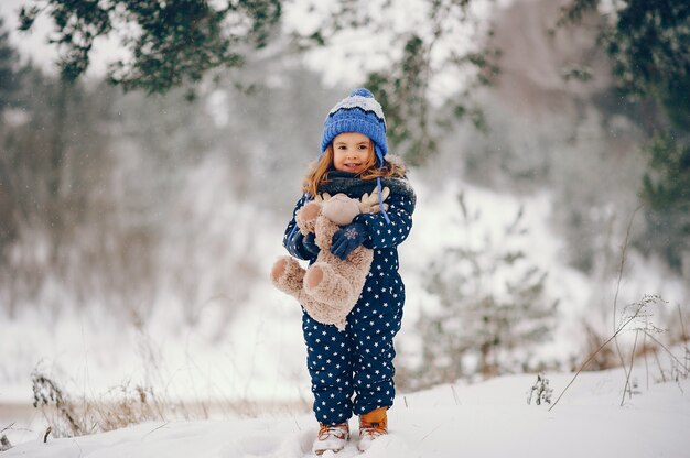 Bambina in un cappello blu che gioca in una foresta di inverno