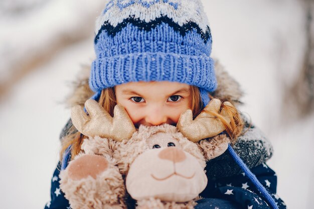 Bambina in un cappello blu che gioca in una foresta di inverno