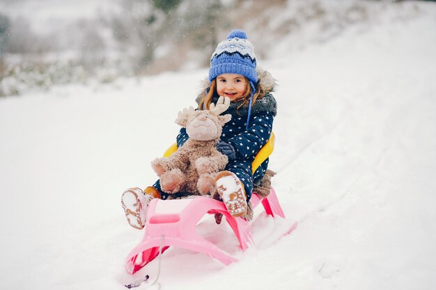 Bambina in un cappello blu che gioca in una foresta di inverno