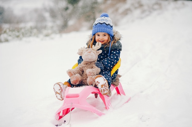 Bambina in un cappello blu che gioca in una foresta di inverno