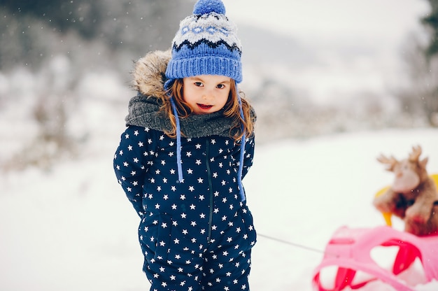 Bambina in un cappello blu che gioca in una foresta di inverno