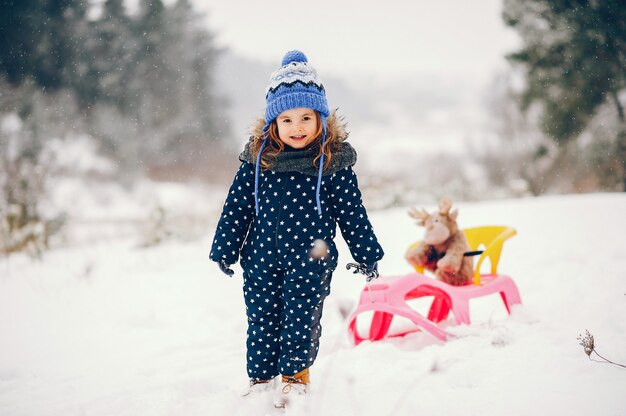 Bambina in un cappello blu che gioca in una foresta di inverno