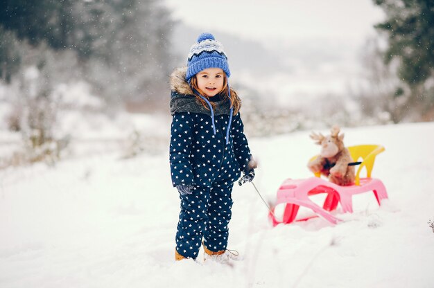 Bambina in un cappello blu che gioca in una foresta di inverno