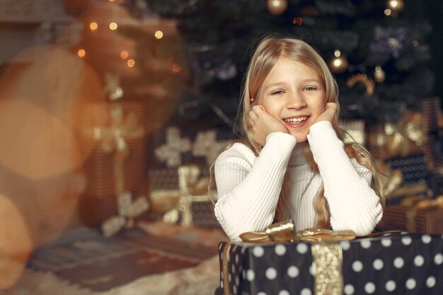 Bambina in un maglione bianco vicino all'albero di Natale con il presente