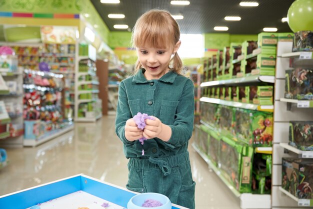 Bambina positiva che scolpisce con il plasticine in negozio di giocattoli