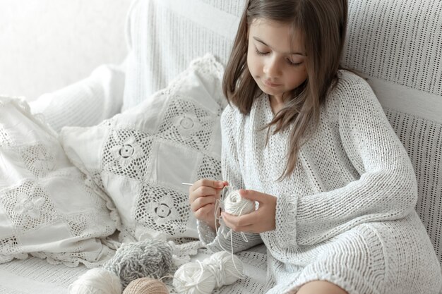 Bambina seduta sul divano con fili, concetto di tempo libero domestico, uncinetto.