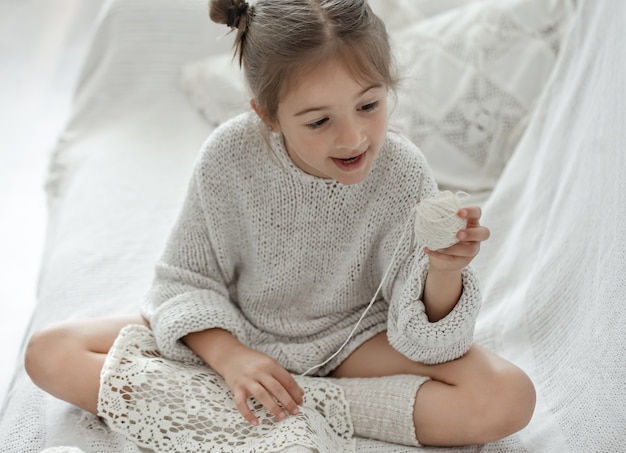 Bambina seduta sul divano e imparare a lavorare a maglia, concetto di tempo libero a casa.