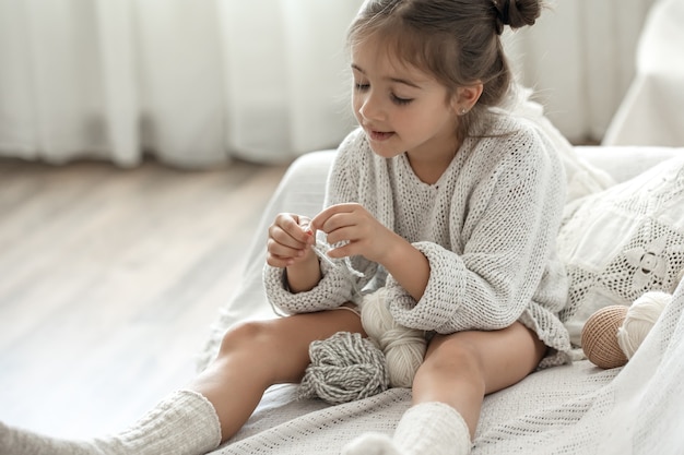 Bambina seduta sul divano e imparare a lavorare a maglia, concetto di tempo libero a casa.