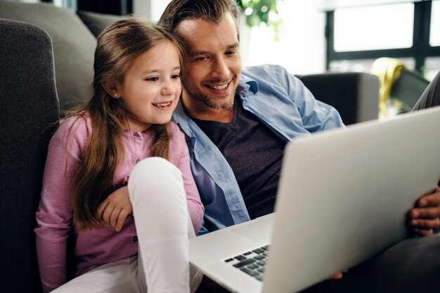 Bambina sorridente e suo padre che usano il laptop mentre ci si rilassa in soggiorno