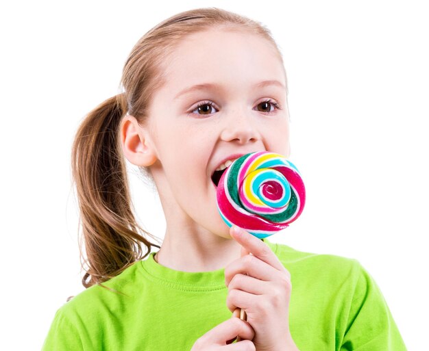 Bambina sorridente in maglietta verde che mangia caramelle colorate - isolato su bianco.