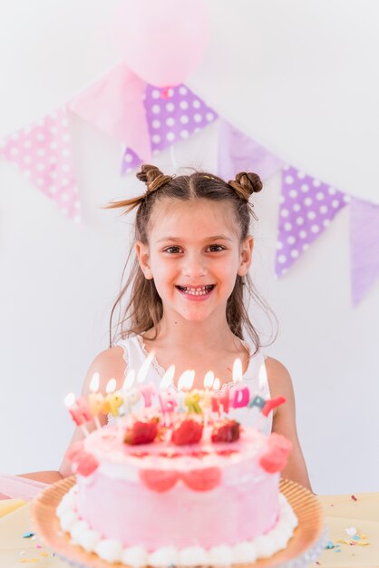 Bambina sorridente sveglia che si leva in piedi vicino alla torta di compleanno