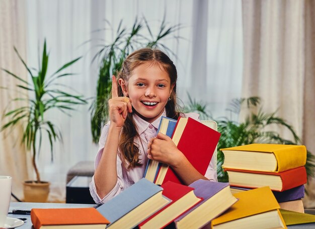 Bambina sveglia al tavolo con molti libri colorati.