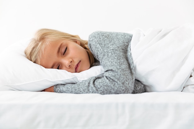 Bambina sveglia che dorme sul cuscino bianco in pigiama grigio che ha sogni piacevoli