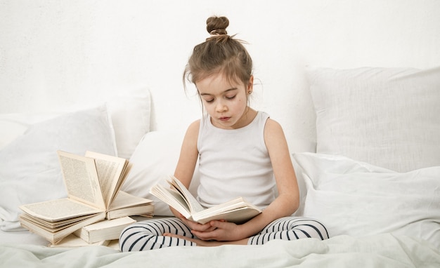 Bambina sveglia che legge un libro sul letto in camera da letto. Il concetto di educazione e valori familiari.