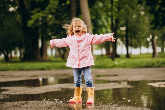 Bambina sveglia che salta nella pozza in un tempo piovoso