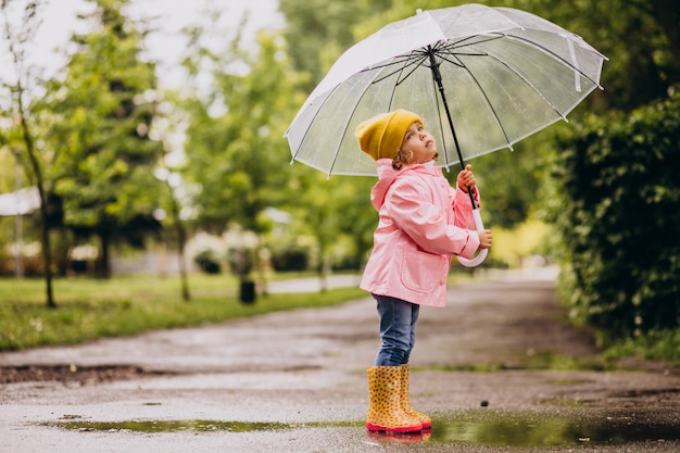 Bambina sveglia che salta nella pozza in un tempo piovoso