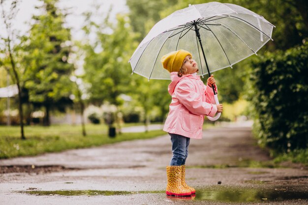 Bambina sveglia che salta nella pozza in un tempo piovoso