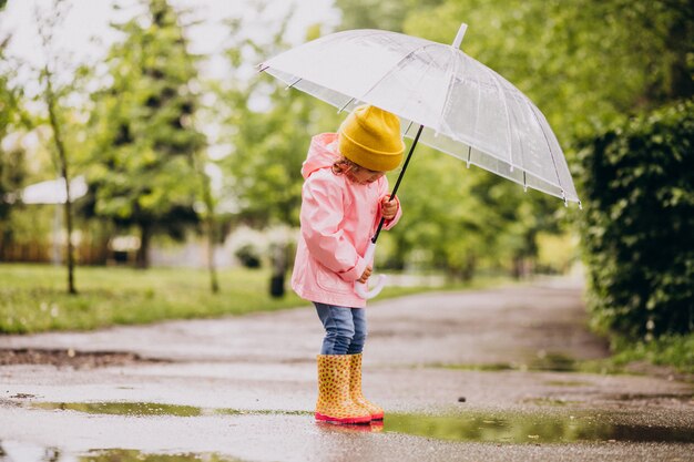 Bambina sveglia che salta nella pozza in un tempo piovoso