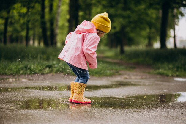 Bambina sveglia che salta nella pozza in un tempo piovoso