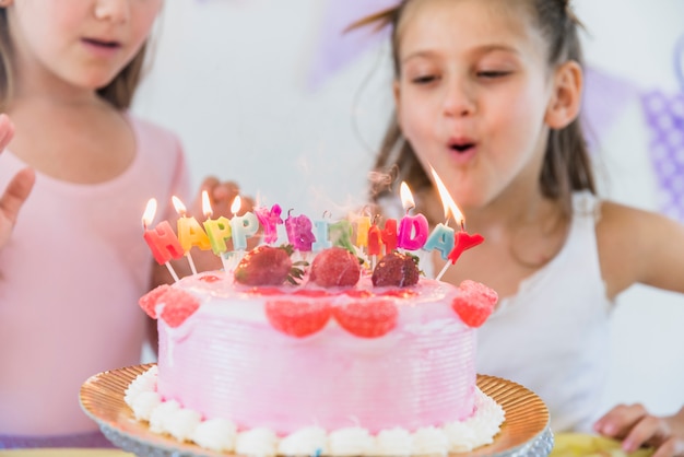 Bambina sveglia che soffia le candele multicolori sulla torta di compleanno
