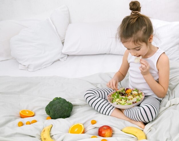 Bambina sveglia con frutta e verdura sulla luce.