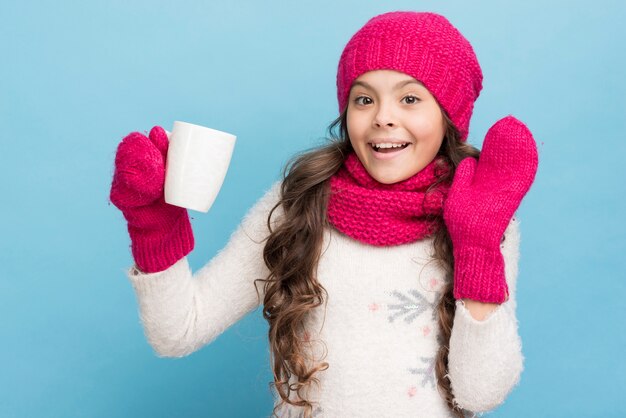 Bambina sveglia con i guanti e cappello che tiene una tazza