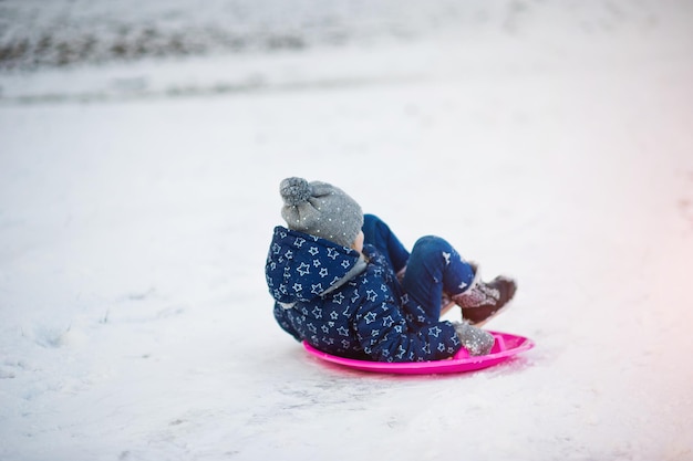 Bambina sveglia con le slitte del piattino all'aperto il giorno di inverno