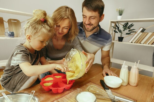 Bambina sveglia ed i suoi bei genitori che preparano la pasta per la torta in cucina a casa