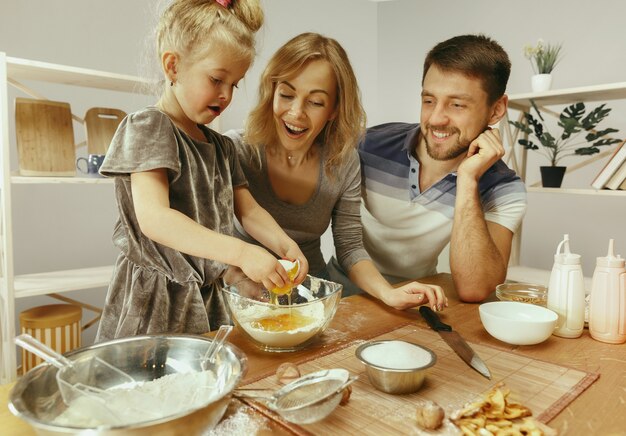 Bambina sveglia ed i suoi bei genitori che preparano la pasta per la torta in cucina a casa