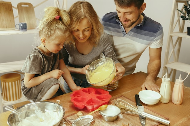 Bambina sveglia ed i suoi bei genitori che preparano la pasta per la torta in cucina a casa