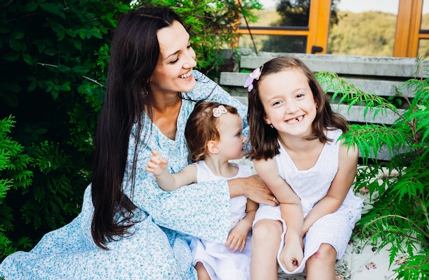 Bambine divertenti siedono negli abbracci della madre sulle orme circondate dalla vegetazione