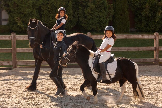 Bambini a figura intera che imparano a cavalcare